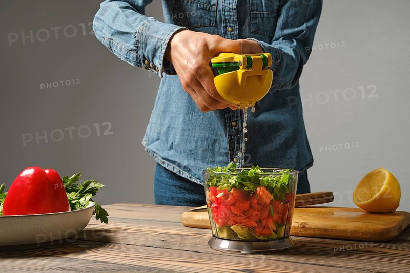Unrecognizable woman using manual juicer to squeeze lemon into blender bowl