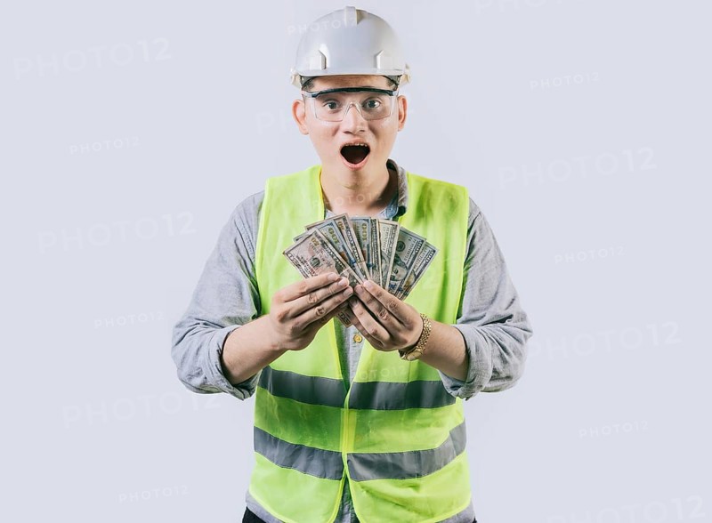Surprised engineer in helmet holding money isolated. Amazed male engineer holding banknotes on isolated background