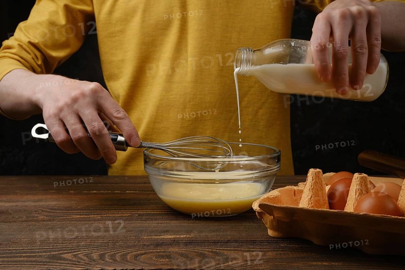 Pouring milk in a bowl with eggs for omelette