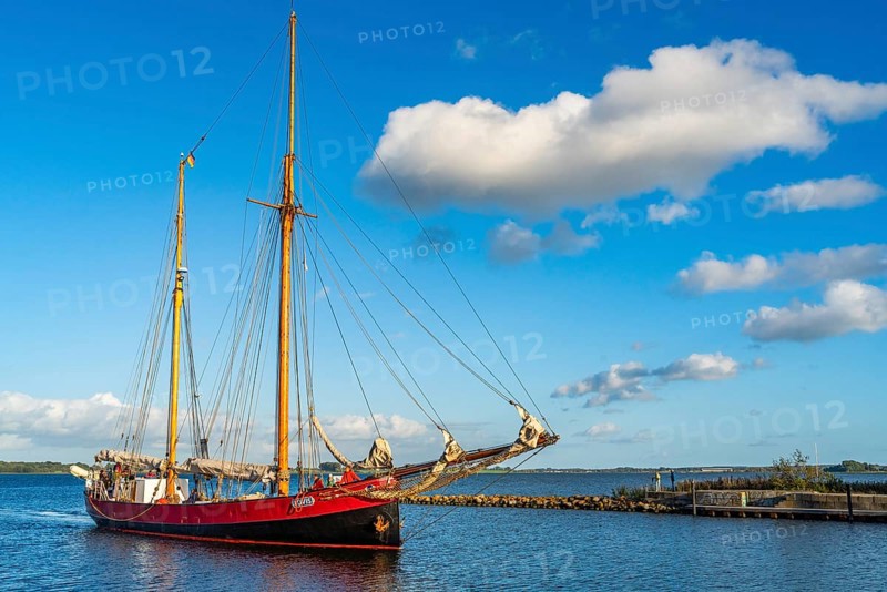 Red traditional sailing boat sails from the Greifswalder Bodden into the river Ryck