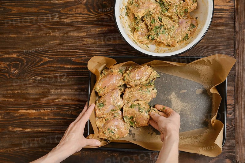 Hands of woman putting chicken thighs in baking tray from a bowl