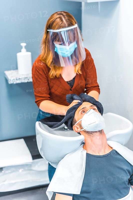 Reopening of hairdressing salons after the Coronavirus pandemic. Hairdresser with face mask and protective screen