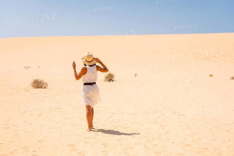 Tourist in white dress and hat walking through the dunes of the Corralejo Natural Park