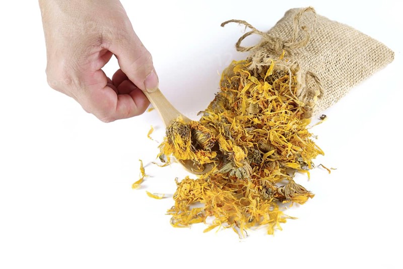 Woman takes a spoonful of dried calendula flowers