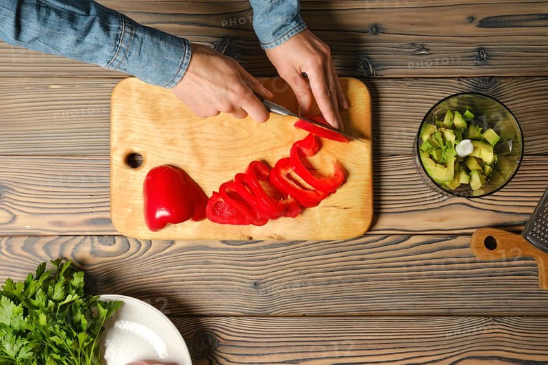 Top view of female hands slicing red bell pepper with kitchen knife
