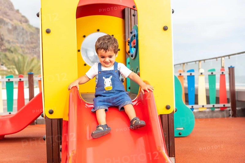 Boy playing in a playground having fun in summer and getting off the squeaker