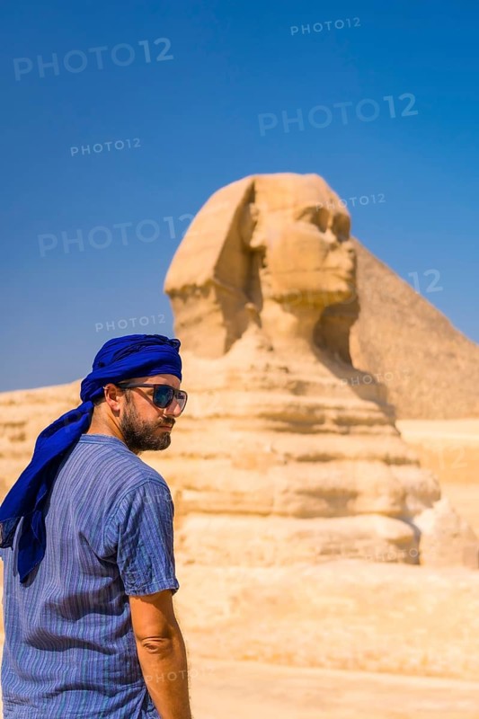 A young tourist enjoying and admiring the Great Sphinx of Giza dressed in blue and a blue turban. Cairo