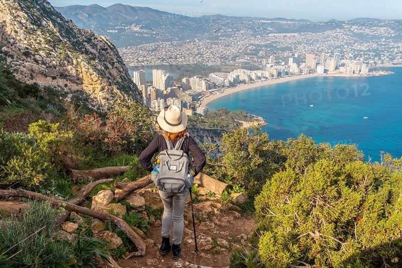 A young hiker on the descent path of the Penon de Ifach Natural Park with the city of Calpe in the background