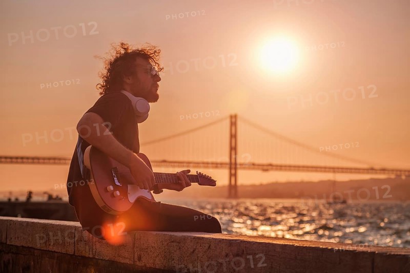 Hipster street musician in black playing electric guitar in the street on sunset
