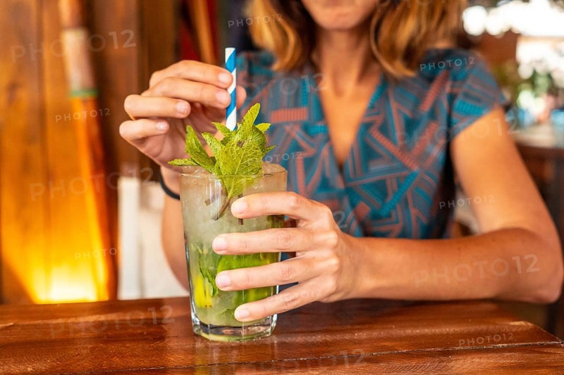 Young girl refreshing herself in the summer with a Mojito cocktail on vacation in a beach bar