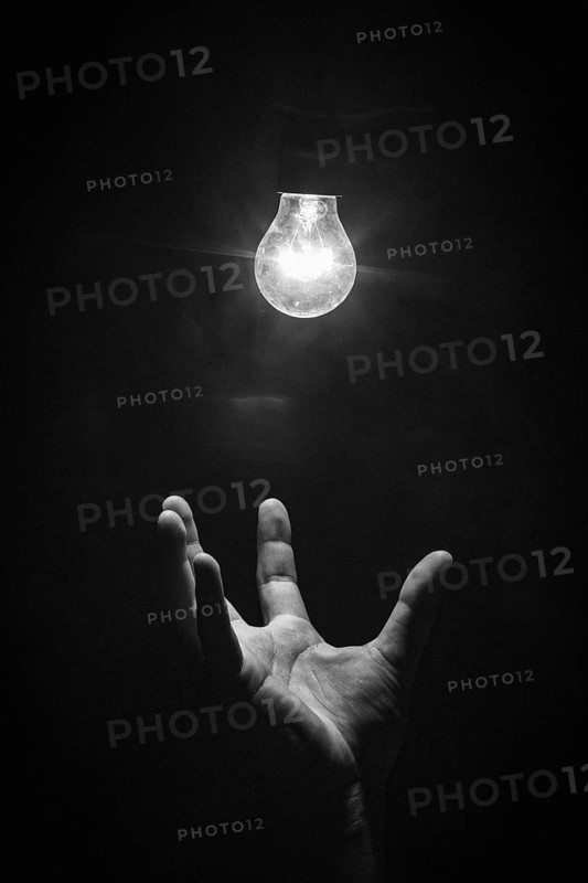 Hand grasps luminous light bulb from below