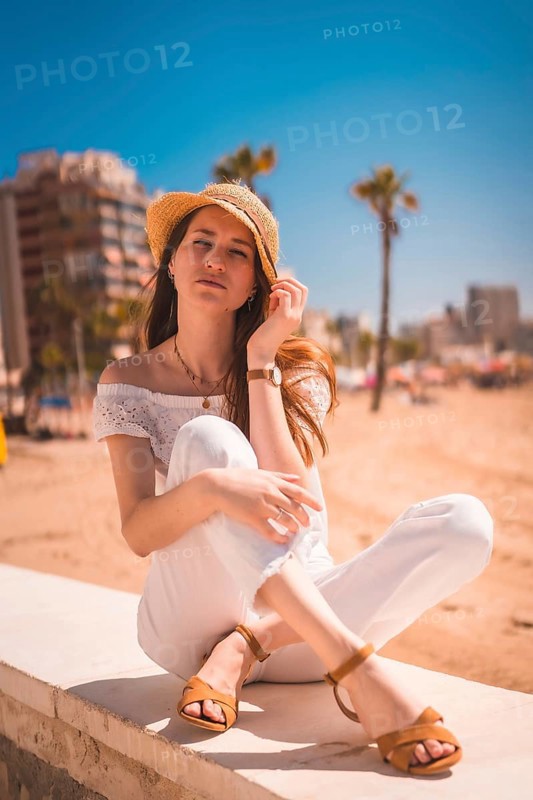 A young red-haired Caucasian girl dressed in white and with a straw hat on the beaches of Calpe