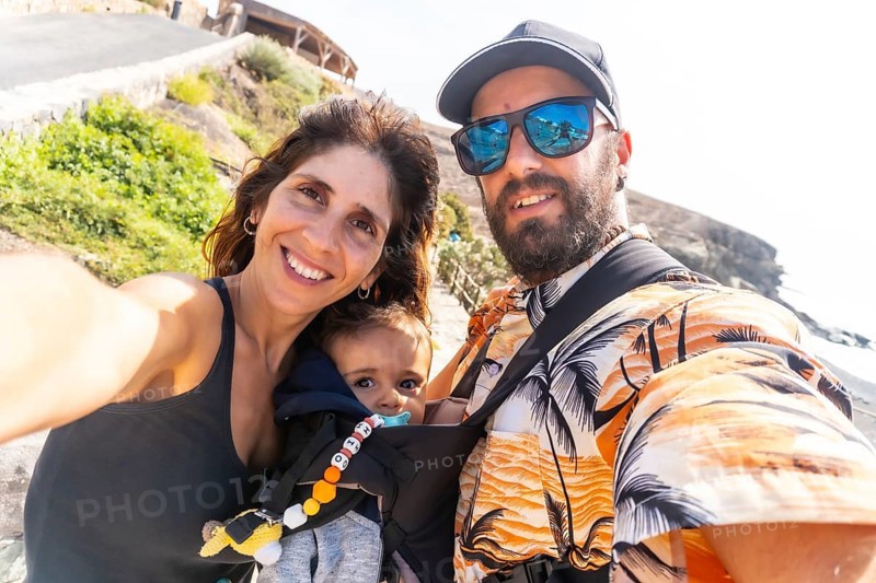 A father with his son in his backpack and the mother on vacation on the beach of Ajuy
