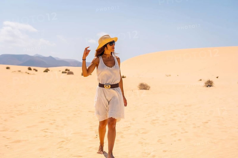 A young European tourist wearing a hat walking through the dunes of the Corralejo Natural Park