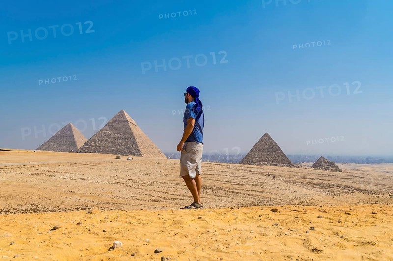Portrait of a young man in a blue turban walking next to the Pyramids of Giza