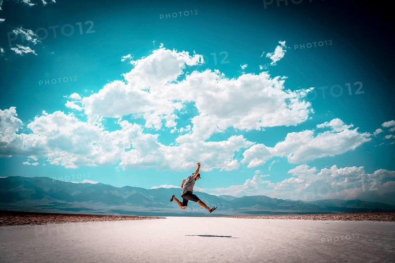 A young man jumping with a blue shirt on the white salt of Badwater Basin