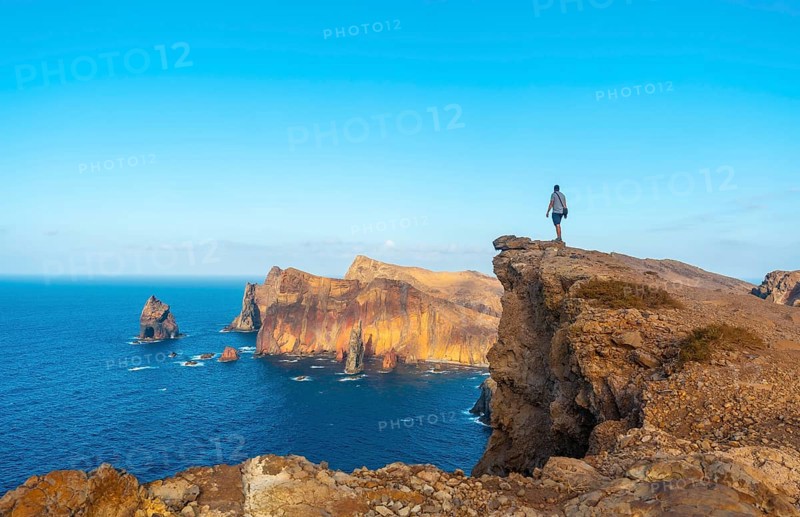 A young man on a cliff at Ponta de Sao Lourenco on the coast with rock formations in summer