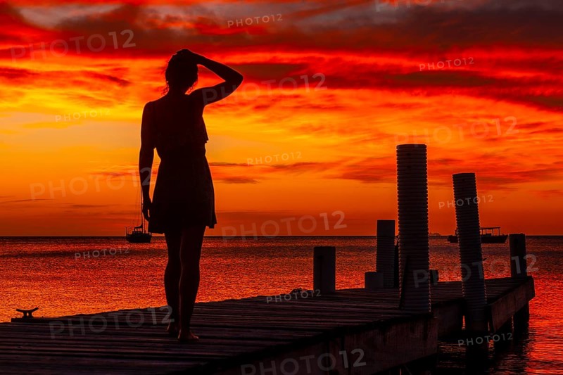 A young woman walking towards the Caribbean Sea in the orange sunset at the West End beach of Roatan. Honduras