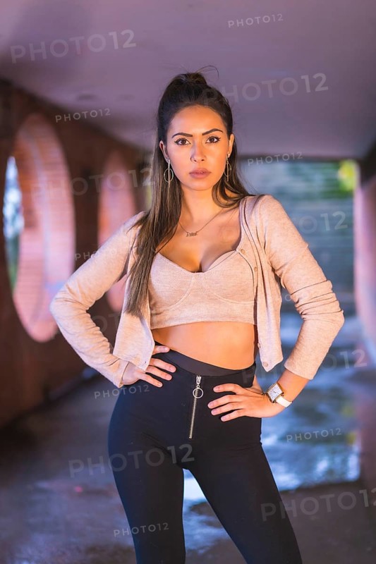 Young caucasian brunette in the city with a beautiful ponytail and a short pink sweater. Street style fashion