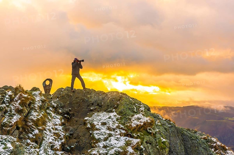 A photographer on top of the mountain in the snowy winter orange sunset
