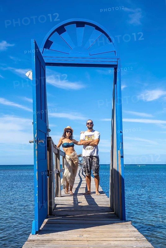 A couple at a blue door on the beach of Sandy Bay on Roatan Island. Honduras