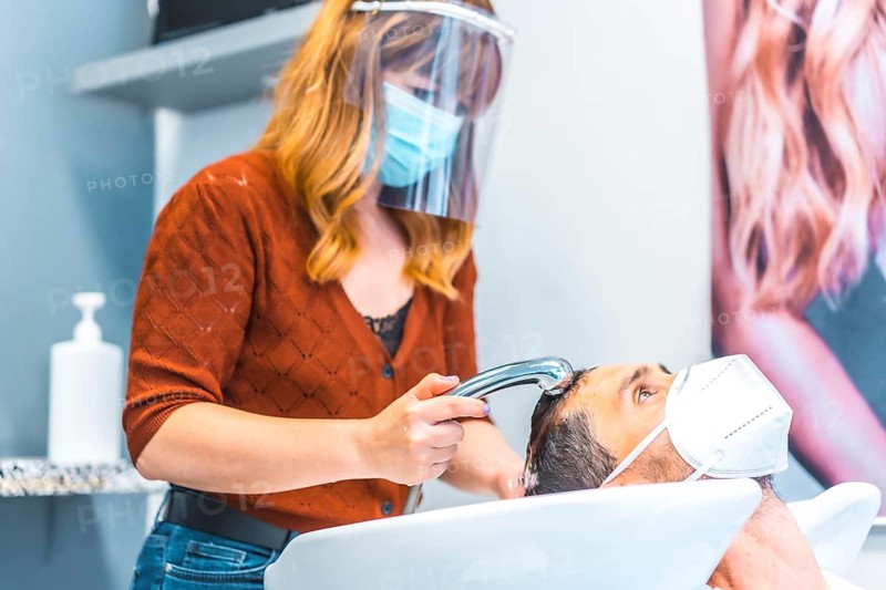 Reopening of hairdressing salons after the Coronavirus pandemic. Hairdresser with face mask and protective screen