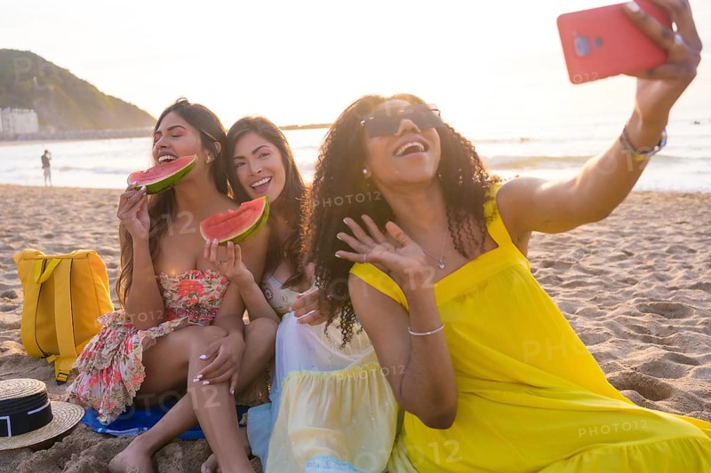 Friends waving while taking a selfie enjoying picnic on the beach during the sunset