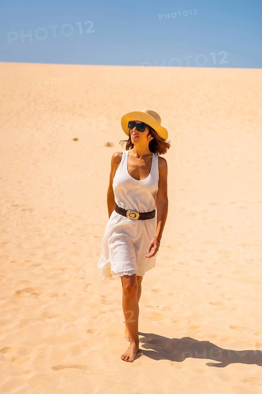 A young tourist in a white dress and a hat walking through the dunes of the Corralejo Natural Park