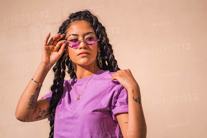 Urban session. Young dark-skinned woman with long braids wearing purple glasses on a plain background