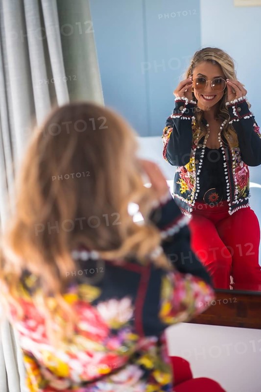 Fashion portrait of a blonde woman putting on her sunglasses in front of a mirror in a hotel