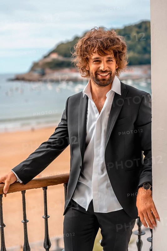 Street style with a young brunette caucasian man in a black suit and a white shirt in a luxurious hotel