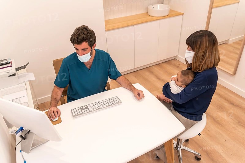 High angle view of a woman with baby in arms in a pediatric appointment sitting and talking with a doctor