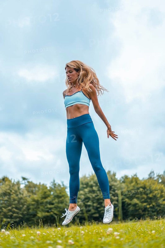Fitness session with a young blonde caucasian woman exercising in nature with a blue maya on her feet and a white short shirt. Squatting and jumping