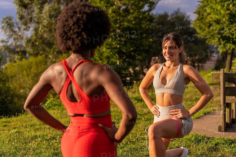 Caucasian blond girl and dark-skinned girl with afro hair doing stretching exercises in a park. Healthy life