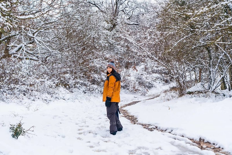 A young woman in a yellow jacket walking along the path of frozen trees. Snow in the town of Opakua near Vitoria in Araba