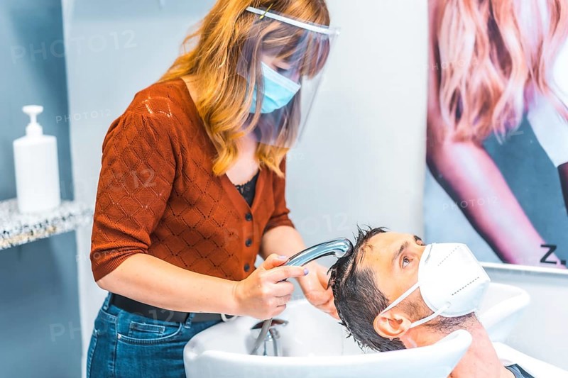 Reopening of hairdressing salons after the Coronavirus pandemic. Hairdresser with face mask and protective screen