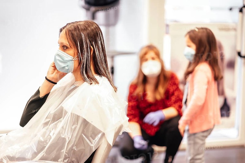 Hairdresser with mask and gloves talking to the client's daughter while the client answers an important call. Reopening with security measures for hairdressers in the Covid-19 pandemic