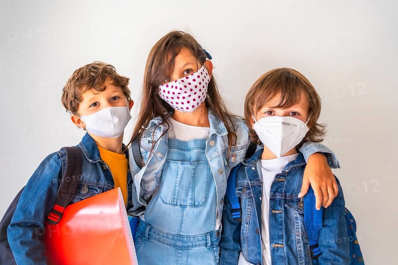 Three children with face masks ready to go back to school. New normality
