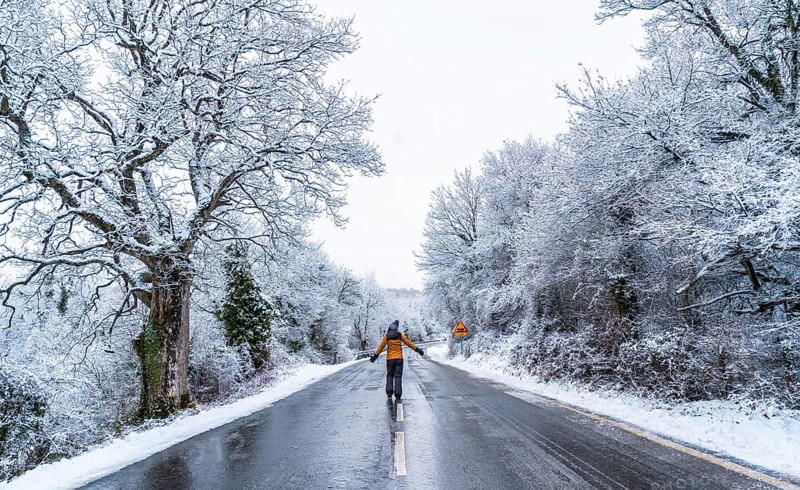 A young woman in a yellow jacket walking along an icy road and denied trees. Snow in the town of Opakua near Vitoria in Araba