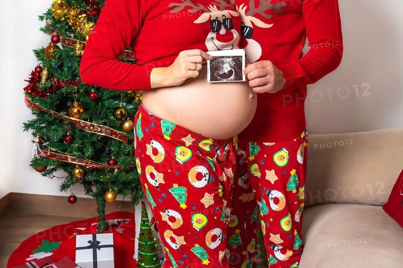 Young couple with red Christmas decorations and clothes having an ultrasound of the new child for the family. Family with pregnant woman