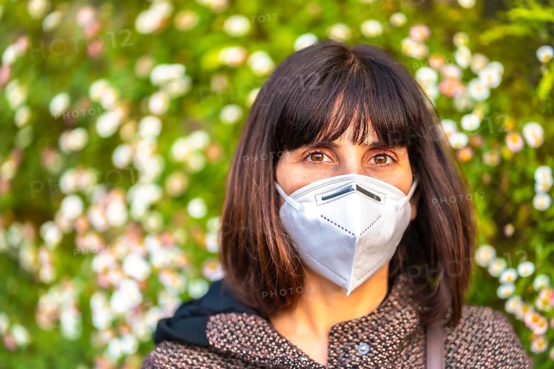 Portrait of a young woman with a mask next to a beautiful daisies. First walks of the uncontrolled Covid-19 pandemic