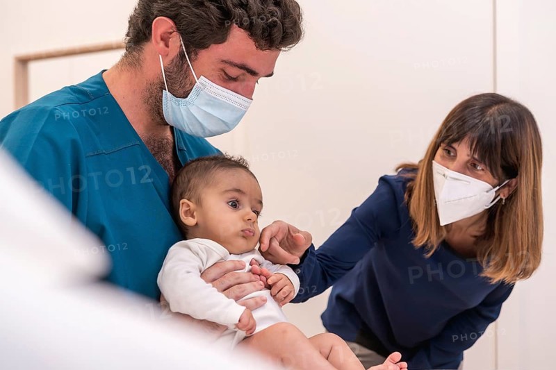 Doctor holding a baby next to his mother during a medical exam