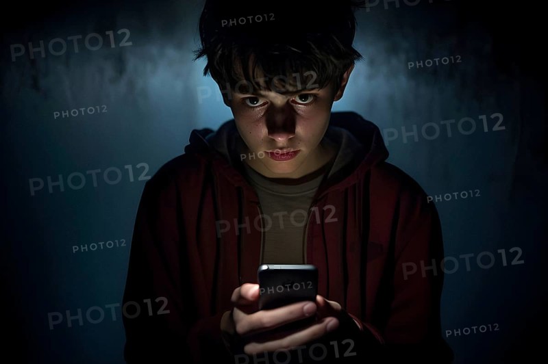 Teenage boy doomscrolling on his smartphone looking exhausted. Dark background. Generative AI