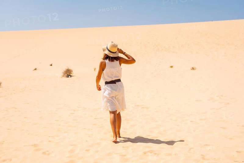Tourist in white dress and hat walking through the dunes of the Corralejo Natural Park