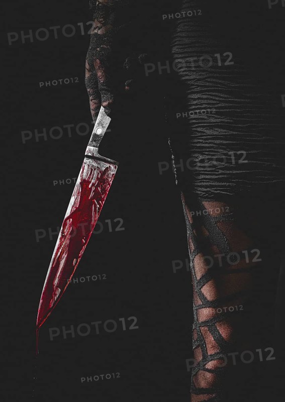 Hand with black lace glove holds bloodstained knife next to woman's leg
