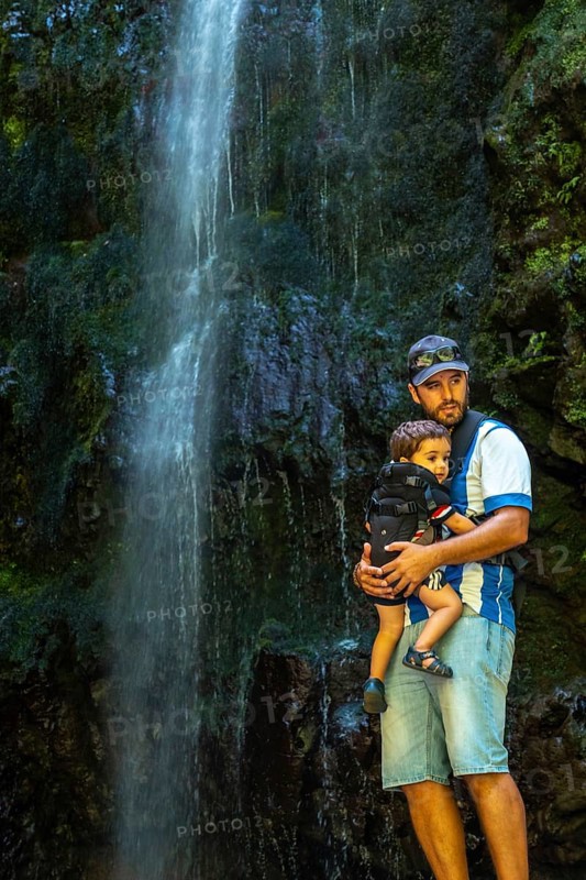 A father with his son in his backpack at the waterfall at Levada do Caldeirao Verde