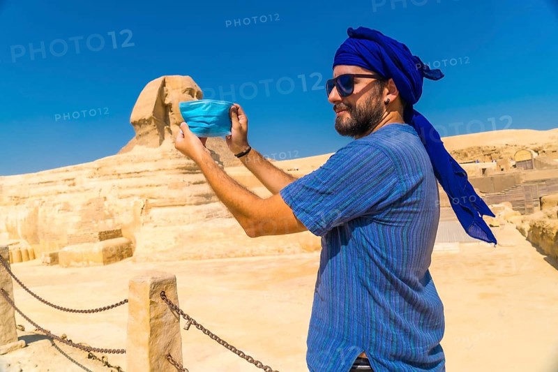A young man putting on the mask facing the Great Sphinx of Giza and the Pyramids of Giza in the background