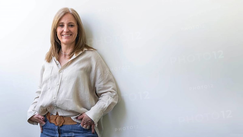 Beautiful caucasian mid aged woman looking at camera leaning on white wall. Copy space