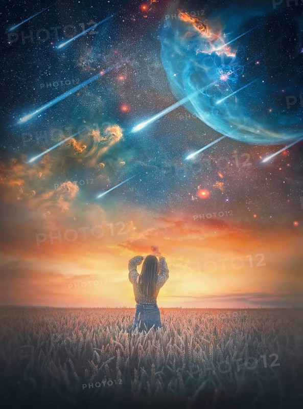 Carefree young woman in the wheat field facing the magical cosmic phenomenon. Wild and free girl rear view portrait at twilight under the starry sky falling comets. Fantastic space scenery