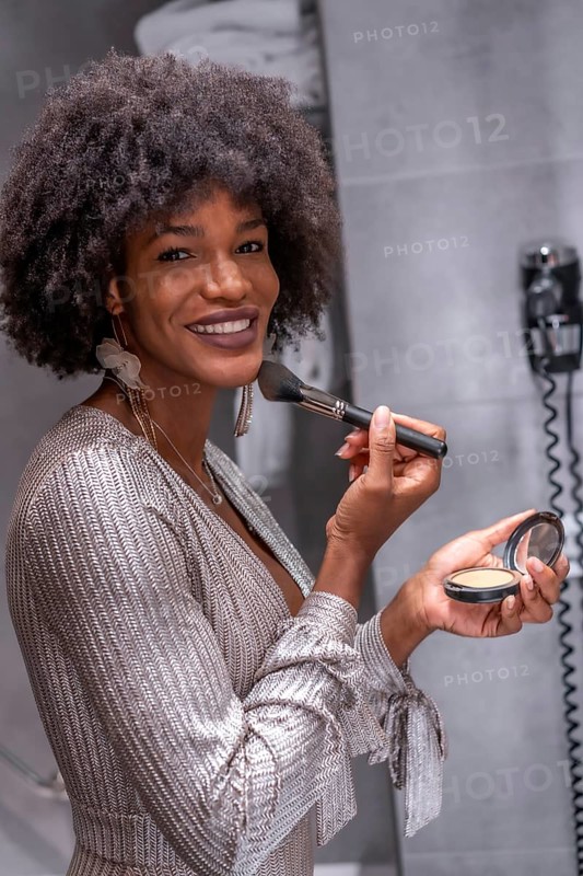 A young black girl with afro hair putting on makeup before the party with a smile. Exclusive party